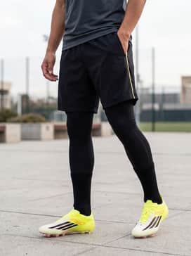 F50 Elite Firm Ground Soccer Cleats – Black compression leggings worn under matching black athletic shorts with a fitted neon-accented moisture-wicking training top.