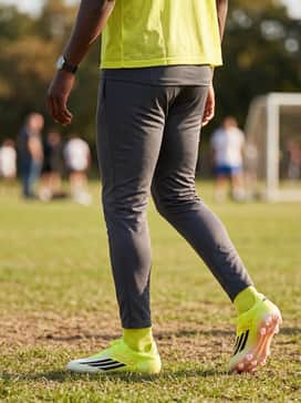 F50 Elite Firm Ground Soccer Cleats – High-visibility solar yellow training bib over a charcoal grey compression base layer and minimalist black track pants.