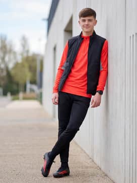 F50 League Mid Cut Firm Ground  Multi Ground Football Boots – A streamlined training outfit consisting of black tapered track pants, a quarter-zip red training top, and a lightweight weather-resistant vest.