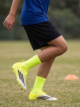 F50 League Mid Cut Firm Ground  Multi Ground Soccer Cleats Kids – A matching team-colored jersey paired with black moisture-wicking soccer shorts and high-performance neon yellow soccer socks to coordinate with the cleats.