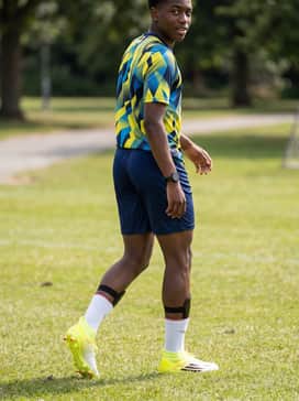 A classic club replica kit featuring navy blue shorts and a vibrant graphic training tee, finished with protective shin guards tucked under white calf-length socks.