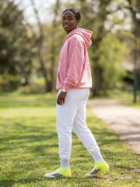 F50 League Mid Cut Firm Ground  Multi Ground Soccer Cleats – Relaxed-fit athletic joggers in white paired with an oversized graphic hoodie that picks up the pink accents of the cleats for a stylish pre-match travel look.