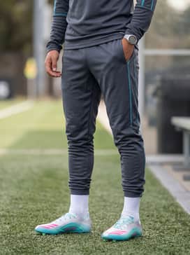 A sleek charcoal grey moisture-wicking tracksuit with teal side-stripe accents, perfect for pre-game warm-ups on the sidelines.