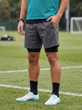 F50 Messi Elite Firm Ground Soccer Cleats – A sleek black compression base layer set worn under a teal training pinnie and charcoal grey 7-inch technical shorts for high-intensity practice sessions.