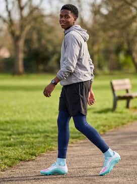 F50 Messi League Firm Ground Multi Ground Football Boots Kids – Navy blue compression leggings worn under black shorts, topped with a lightweight grey hooded windbreaker for cool-weather morning training sessions.