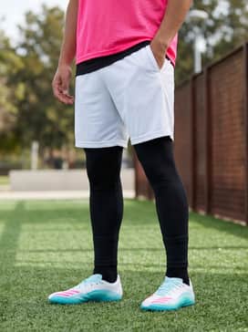 F50 Messi League Firmmultiground Cleats – High-performance matte black compression leggings worn under white technical training shorts, paired with a neon pink training bib for a high-visibility look during drills.