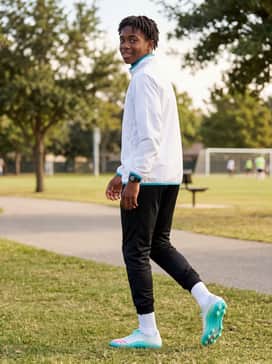 F50 Messi Pro Firm Ground Soccer Cleats – A sleek white windbreaker jacket with cyan accents paired with black soccer joggers for a coordinated look while arriving at the stadium.