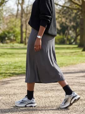 Fade Sneakers – A charcoal grey slip midi skirt paired with a chunky knit black sweater and silver jewelry to lean into the 'wrong shoe theory' fashion trend.