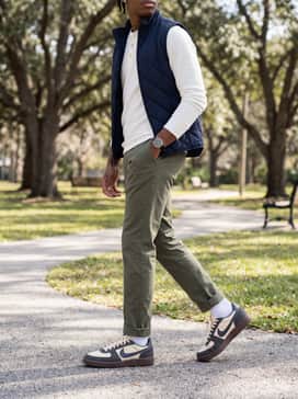 Cuffed olive green chinos worn with a white long-sleeve henley and a navy blue quilted vest for a clean, heritage-inspired outfit.