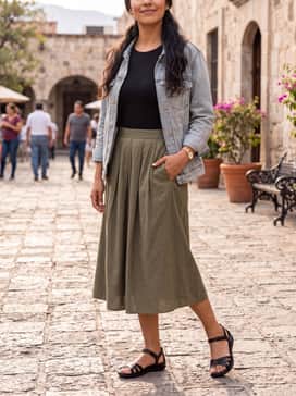A mid-length pleated skirt in an olive earth tone worn with a black tucked-in bodysuit and a light denim jacket for weekend errands.