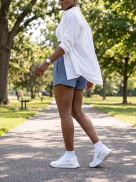 Dusty blue athletic shorts with a white racerback sports bra and a lightweight, unbuttoned linen shirt for a fresh, breathable summer errand outfit.