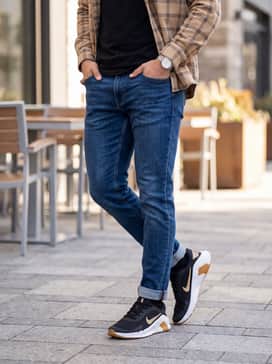 Flex Train – Slim-fit indigo denim jeans with a crisp white crew-neck tee and an unbuttoned tan flannel shirt to complement the gum sole and gold accents.