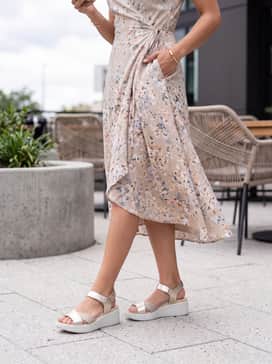 Flowt Wedge Lx – A floral midi wrap dress in pastel tones with delicate gold jewelry to complement the metallic straps of the sandal.
