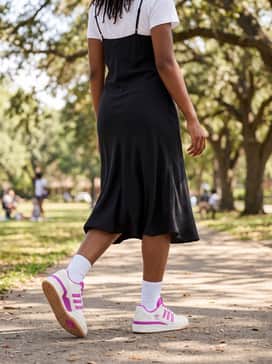 A black midi-length slip dress layered over a plain white t-shirt for a 90s-inspired street style ensemble that balances feminine and sporty elements.