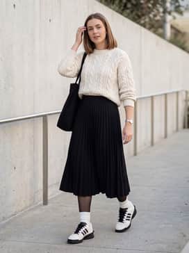 Forum Sq Shoes – A black pleated midi skirt with a chunky cream cable-knit sweater and sheer black tights for a feminine yet edgy contrast.