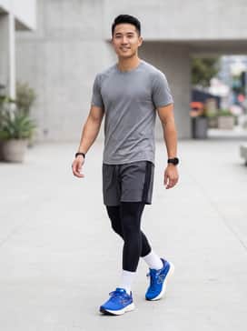Black moisture-wicking compression leggings worn under charcoal grey 7-inch running shorts with a neon-detailed tech tee.