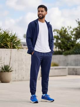 Navy blue tapered track pants paired with a white breathable mesh tank top and a matching lightweight blue windbreaker.