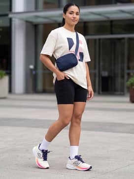 A trendy athleisure ensemble with black high-waisted bike shorts, an oversized cream graphic t-shirt, and a sleek navy crossbody bag.