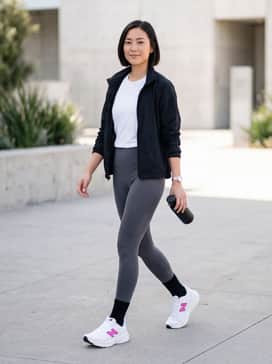 High-waisted charcoal grey compression leggings paired with a matching sports bra and a lightweight, oversized white zip-up windbreaker.