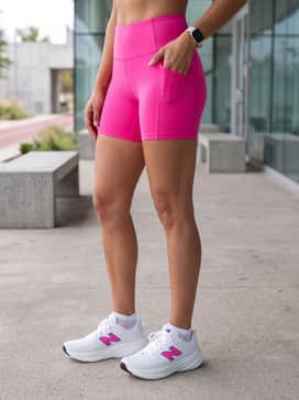 Bright hot pink biker shorts that coordinate with the logo, worn with a loose-fitting white moisture-wicking racerback tank top.