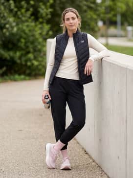 Black tapered joggers with a fitted cream-colored technical long-sleeve shirt and a lightweight quilted vest for cooler outdoor runs.