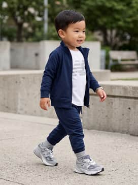 A sporty ensemble featuring navy blue moisture-wicking joggers, a matching zip-up track jacket over a white graphic tee, and grey crew socks for a coordinated athletic look.