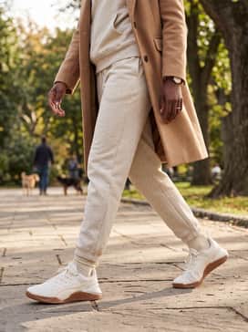 A minimalist travel set consisting of a matching oatmeal-toned fleece jogger and hoodie combo, topped with a structured camel wool coat for added polish.