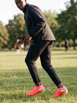 A coordinated warm-up look featuring a lightweight black windbreaker jacket and slim-fit joggers with a subtle reflective trim that mirrors the silver Puma logo.