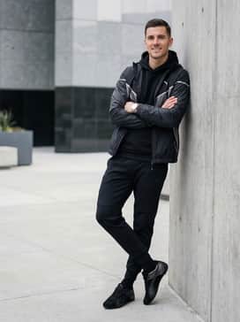 A modern athleisure outfit pairing black technical fleece joggers with a fitted black performance hoodie and a lightweight silver-accented windbreaker.