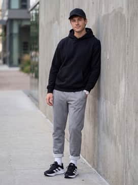 A relaxed athleisure ensemble with heather grey tech-fleece sweatpants, a matching black oversized hoodie, and a structured baseball cap for a comfortable travel day.