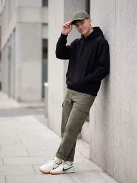 Slim-fit olive green cargo trousers and a heavyweight black hoodie, finished with a matching green baseball cap for a cohesive streetwear look.