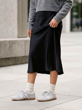 A black satin midi slip dress layered with a cropped grey cashmere sweater to balance feminine and sporty elements.