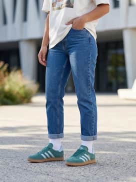 Slim-fit cropped blue jeans paired with an oversized white graphic tee and a tan trench coat for a weekend city stroll.