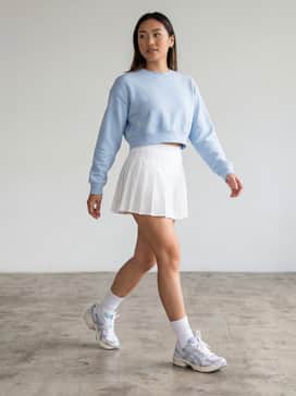 A white pleated tennis skirt paired with a baby blue cropped sweatshirt and white crew socks for a fresh, athletic vibe.