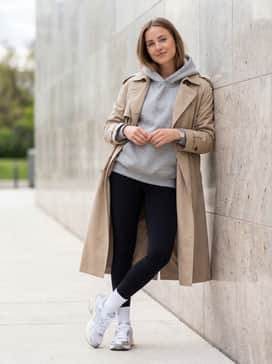 Black high-waisted leggings worn with a grey oversized hoodie and a beige trench coat for a sophisticated yet comfortable travel look.