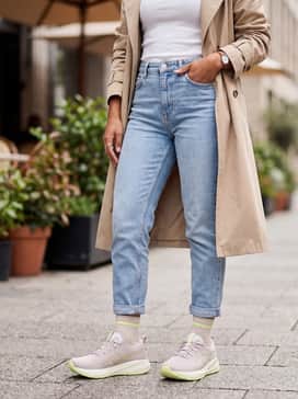 Gelcumulus 27 Wide – Light-wash tapered jeans with a tucked-in white rib-knit tee and a beige trench coat for a sophisticated off-duty streetwear look.