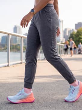 Gelcumulus 28 Sunny Sizzle – A casual athleisure ensemble with charcoal grey tapered joggers, a moisture-wicking pale mint tank top that echoes the shoe's upper, and a vibrant pink baseball cap.