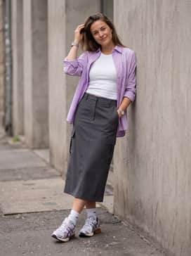 Gelkinetic Fluent – A charcoal grey cargo midi skirt styled with a fitted white ribbed tank top and an unbuttoned lilac button-down shirt.