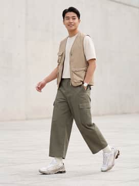 Gelkinetic Fluent – Wide-leg olive cargo pants paired with a cream technical tee and a tan utility vest for a functional gorpcore aesthetic.