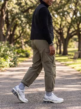 Baggy olive-toned cargo pants styled with a black fitted turtleneck and a technical utility vest for a modern, functional utilitarian outfit.
