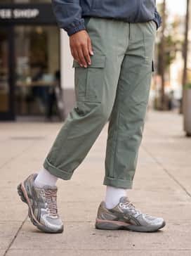 Sage green technical cargo pants with a cinched ankle, a charcoal grey windbreaker, and high-quality white crew socks pulled up to showcase the shoe's silhouette.