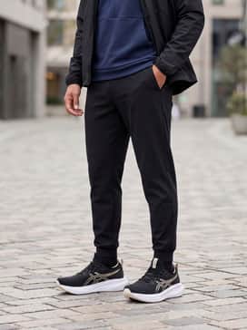 Gelnimbus 28 Extra Wide – Tapered black joggers paired with a fitted navy blue quarter-zip tech fleece and a lightweight waterproof running jacket.