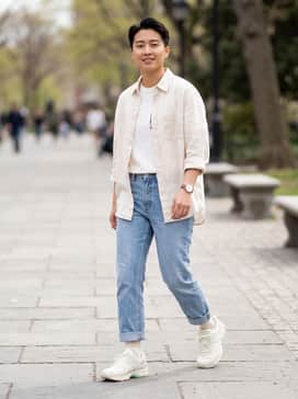 Light-wash straight-leg jeans paired with a vintage graphic tee and an unbuttoned cream linen shirt for a relaxed, layered look.