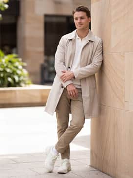 Khaki tapered trousers with a tucked-in white polo shirt and a light beige trench coat for a sophisticated urban commuter aesthetic.