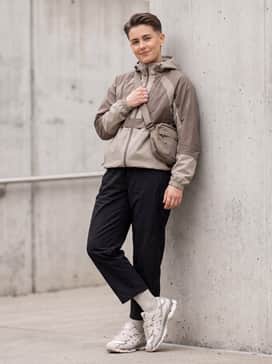 Black nylon track pants, a technical windbreaker in earth tones, and a matching crossbody sling bag for a functional Gorpcore look.