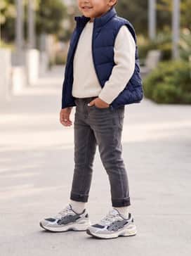 Gelnyc Preschool – Slim-fit denim jeans with a cuffed hem, worn with a cream-colored knit sweater and a navy blue puffer vest for a clean, autumnal look.