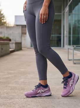 Gelresolution X Wide – Dark charcoal high-waisted leggings worn with a slightly cropped white long-sleeve tech shirt and a navy baseball cap for a post-workout look.