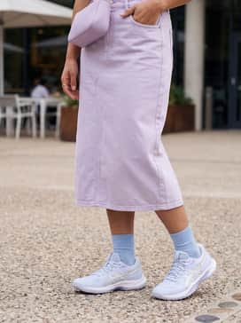 Geltactic 13 – A relaxed streetwear outfit featuring light-wash tapered jeans, a cropped cream-colored graphic t-shirt, and a small lilac crossbody bag to tie the color scheme together.