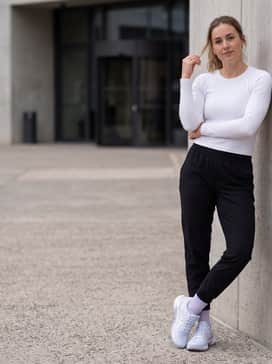 A sleek gym-to-errands ensemble with black technical joggers, a fitted ribbed white long-sleeve top, and gold stud earrings to highlight the shoe's metallic detailing.