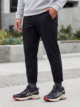 Gelventure 11 Extra Wide – Tapered black joggers paired with a light grey performance hoodie and a utility vest for a modern techwear-inspired street look.
